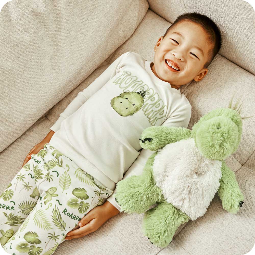 Image 87: Child smiling with a Warmies Stuffed Animal while wearing Dinosaur Pajamas - Warmies USA